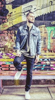 A confident person wearing a bold jacket from The Flyest Survivor, standing against a graffiti wall.