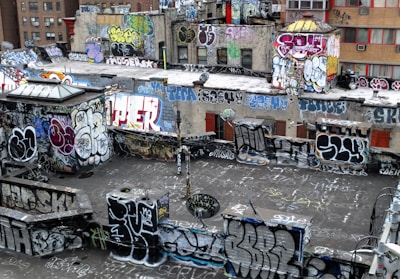 A rooftop densely covered in vibrant graffiti art with various styles and colors. The walls and surfaces are filled with tags, throw-ups, and large murals, displaying the urban art culture. The buildings are in an urban environment with visible windows and some air conditioning units.