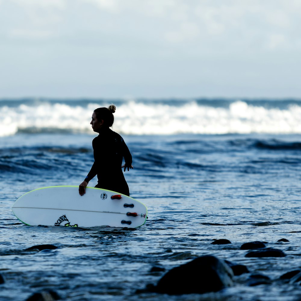 woman holding white surfboard on body of water