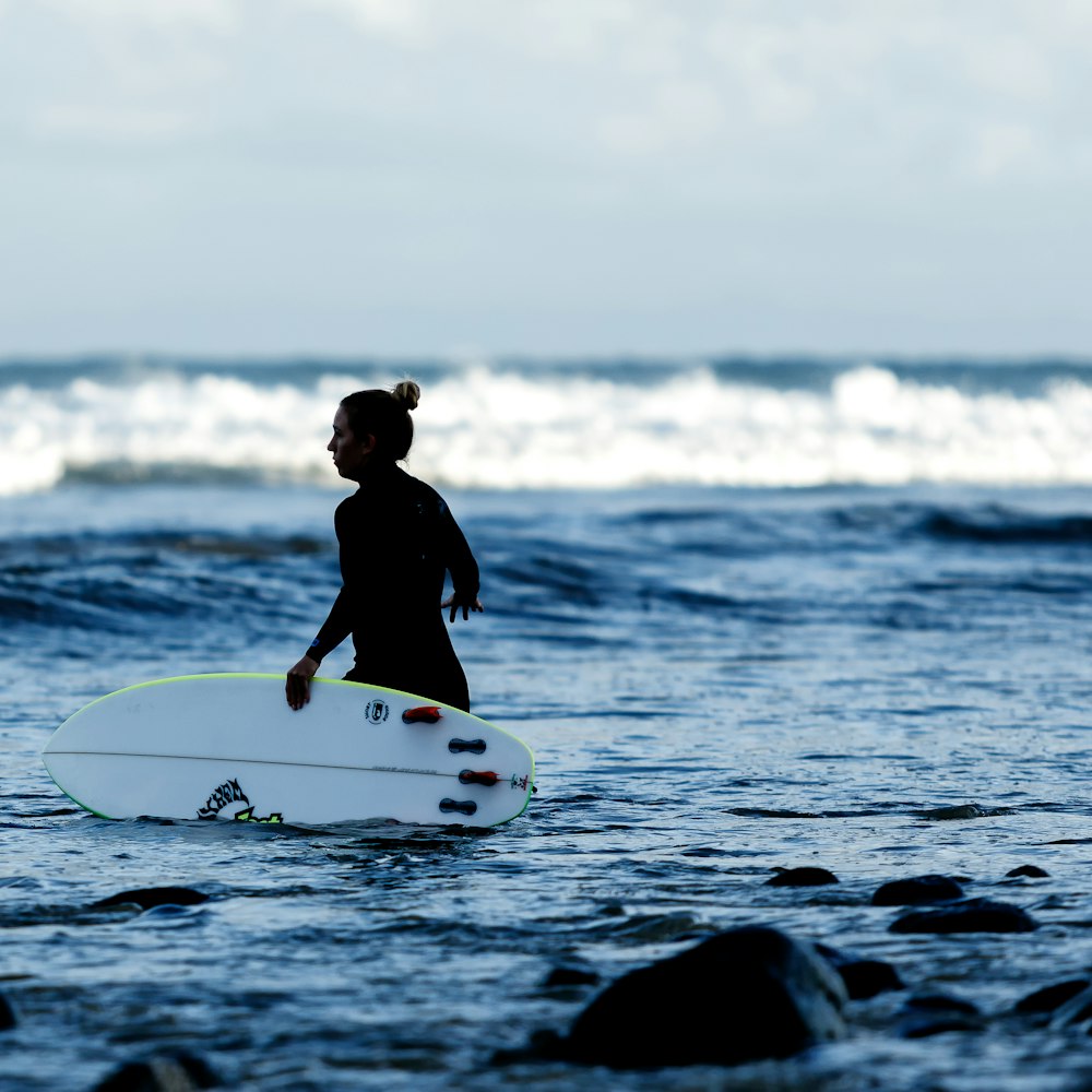 Mujer sosteniendo tabla de surf blanca en el cuerpo de agua