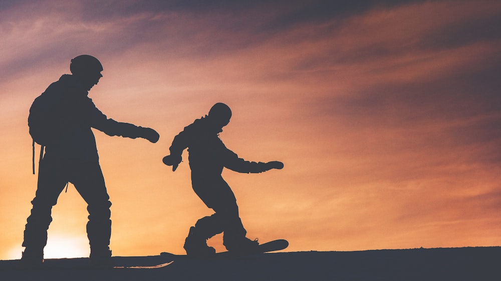 silhouette photo of two person riding on snowboard
