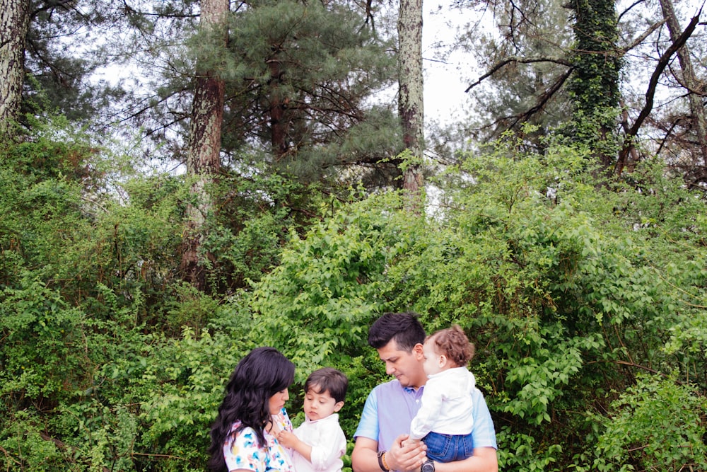 homme et femme portant des enfants debout à côté de plantes vertes pendant la journée