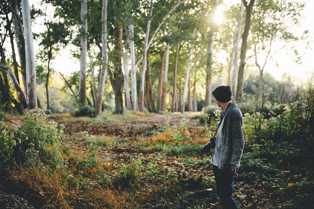 man with black camera standing near green trees during daytime