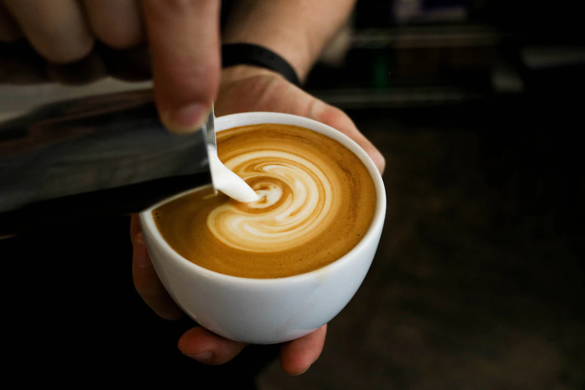 A barista's hand pouring steamed milk into a cortado, forming latte art in low light