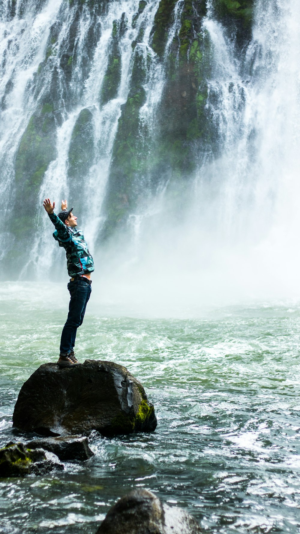 man standing on black rock surrounded body of water