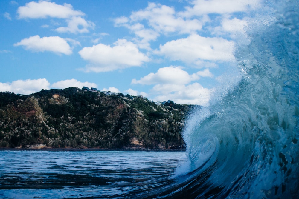 Fotografía de primer plano de la ola del mar bajo las nubes blancas y el cielo azul