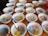 Several white bowls containing colorful shaved ice in shades of blue, pink, and yellow are arranged on a wooden table. Each bowl has a metal spoon resting inside, and the surface of the table is visible between the bowls. The setting appears casual and ready for serving.