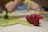 A close-up of a tabletop board game, featuring a red dragon-shaped game piece in focus on a square tile. In the background, a green meeple and another hand are slightly blurred, indicating gameplay. The surface is light-colored, and the scene conveys an intimate setting of game play.