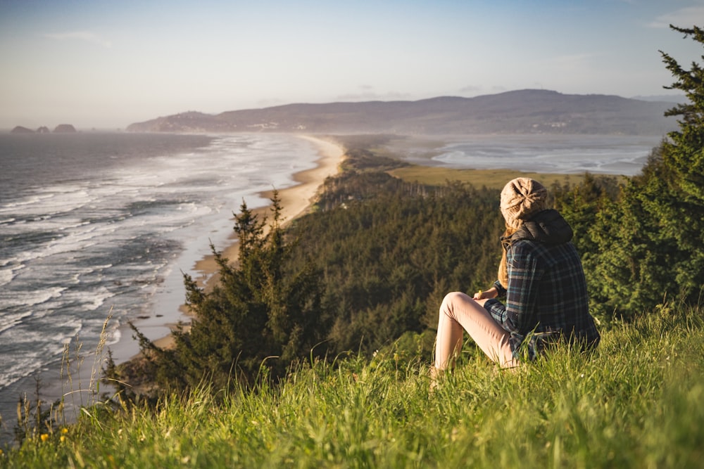 Person, die tagsüber auf einem Hügel in der Nähe des Ozeans sitzt