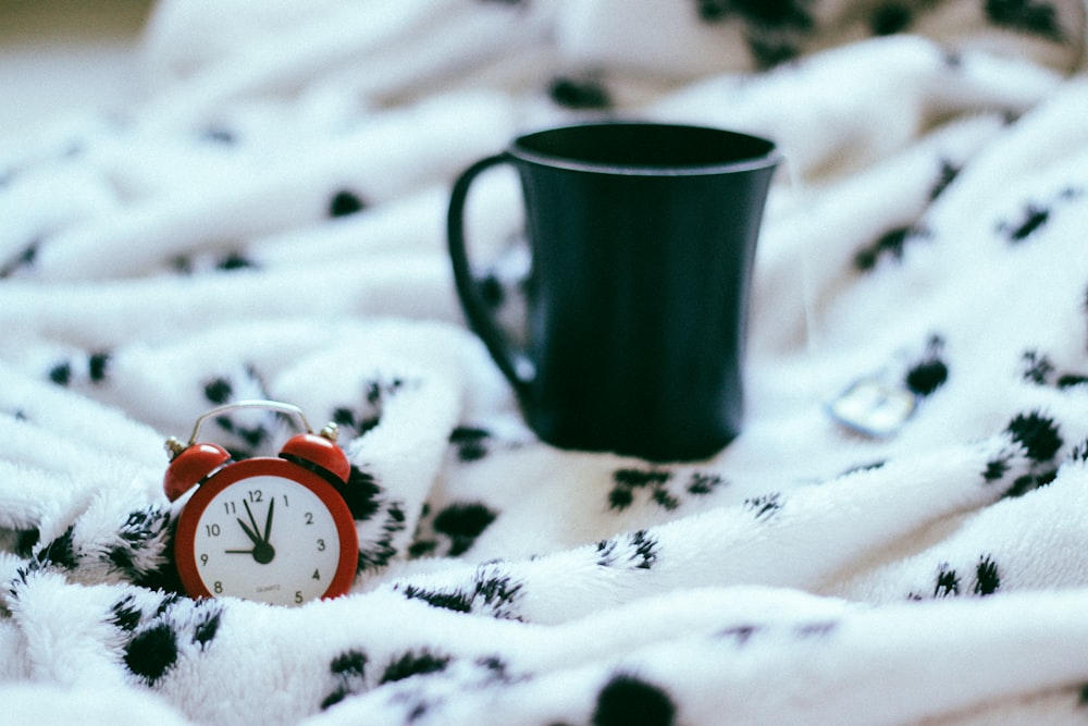 green ceramic mug near analog alarm clock