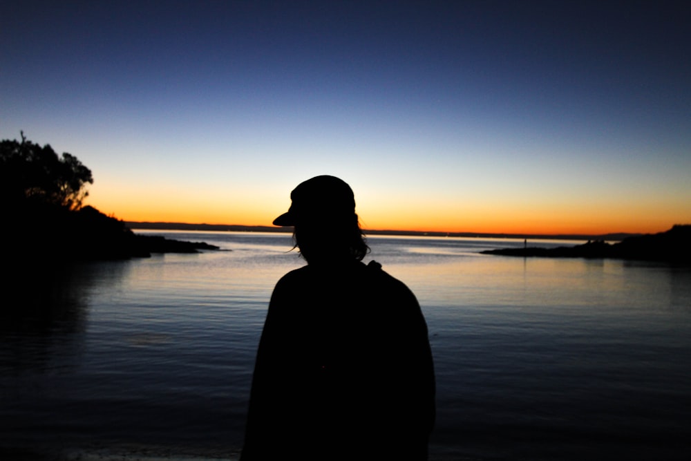 man standing near body of water silhouette photography