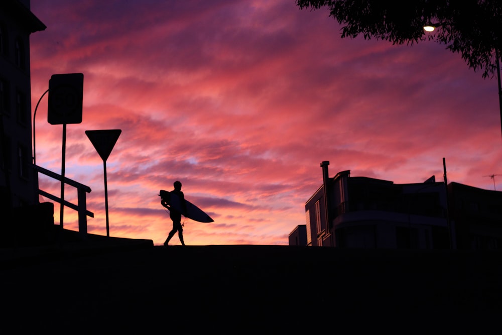 silhouette photography of man walking with a surfboard