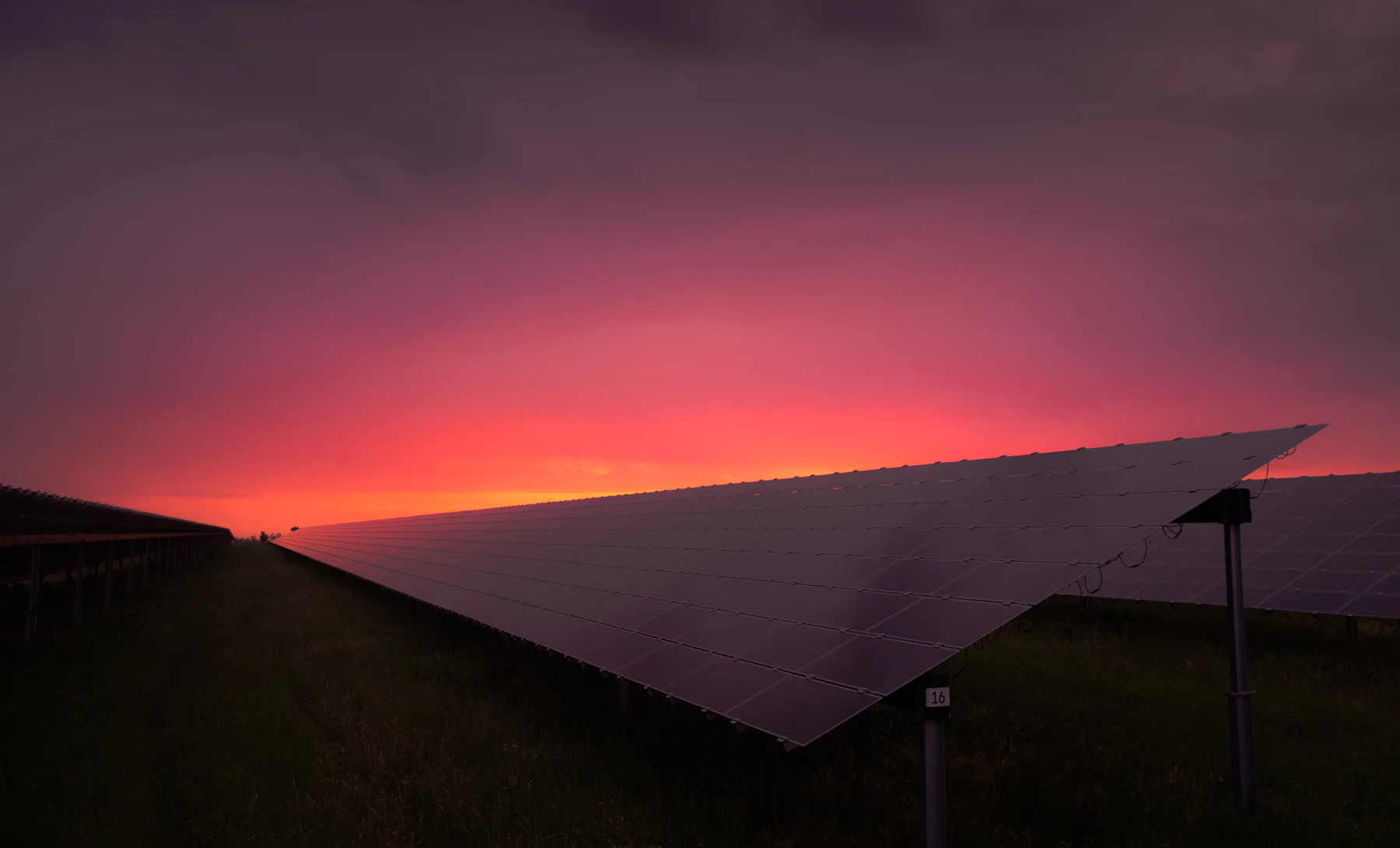 Painéis solares sob céu de entardecer em tons de vermelho e rosa