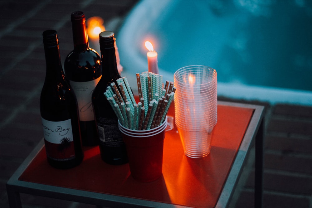 四角い赤いテーブルの上のカップとキャンドルの近くに3本のワインボトル