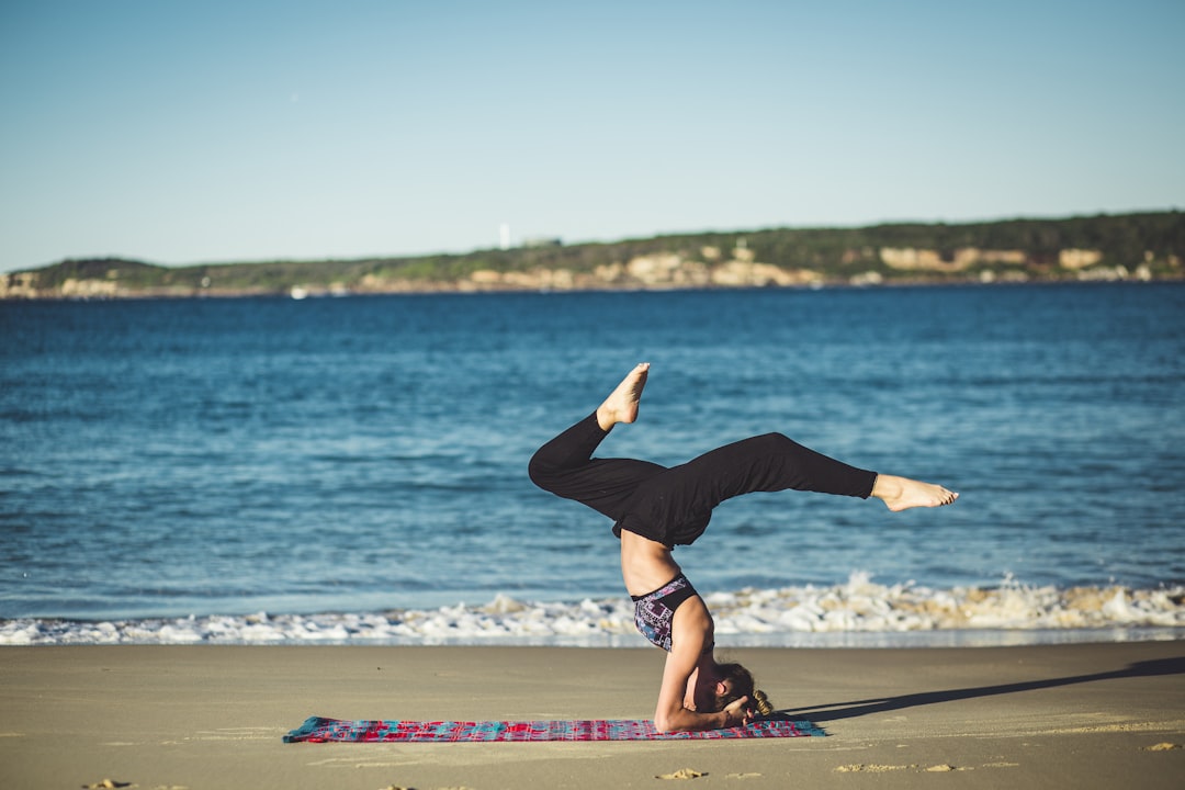 A woman doing yoga on a pink and blue yoga mat by the ocean