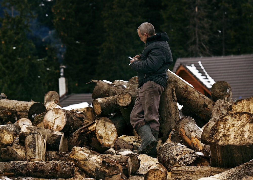 man in black jacket and brown pants sitting on brown log during daytime