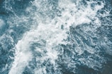 A dynamic top-down view of turbulent water, capturing the movement and texture of foamy waves and dark, deep water.