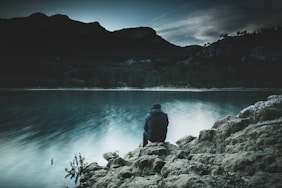 a man sits on a rock staring across a lake at dusk