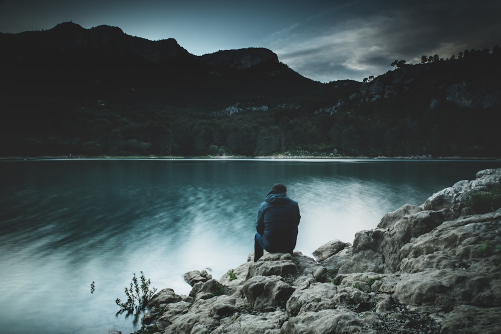 夕暮れの湖の向こうに岩の上に座り、見つめる男