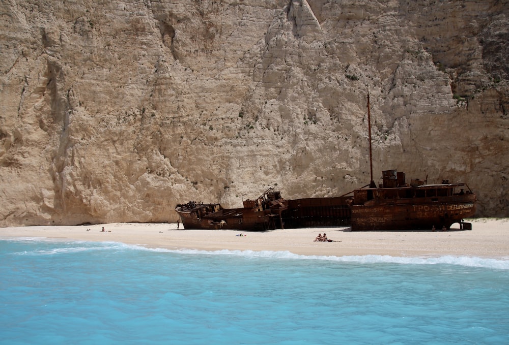 group of people on seashore near ship near mountain at daytime