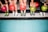 Five people standing side by side are holding colorful bowling balls in their hands. They are wearing bowling shoes with various designs, and their feet are positioned on a tiled floor with a mixture of blue and black tiles.