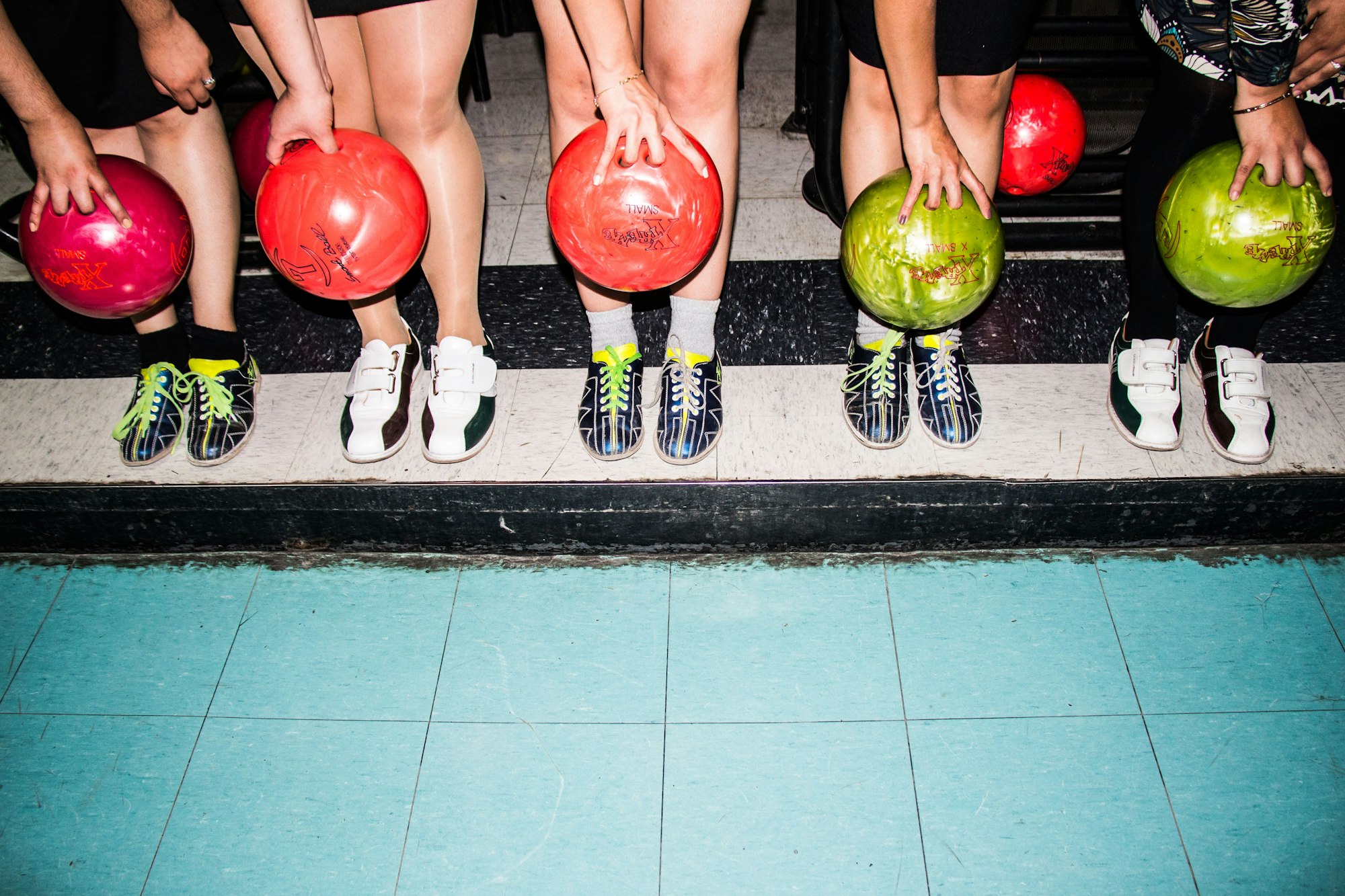 Group of people holding ten pin bowling balls in front of their feet