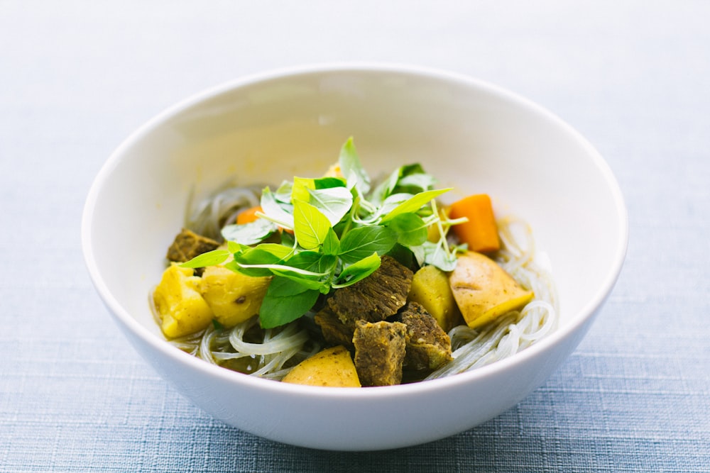 Cuenco redondo de cerámica blanca con lonchas de carne y verduras sobre superficie gris