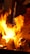 Vivid flames erupt from a fire pit, surrounded by individuals engaged in a ritual. They wear traditional attire and seem to be participating in a spiritual or religious ceremony.
