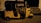 A yellow auto rickshaw is parked on a dimly lit street next to a building with steps leading to an entrance. The vehicle has a black roof and three wheels, with some text visible on its side.