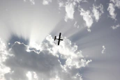 Silhouette of a small aircraft flying above a mountain range at sunset.