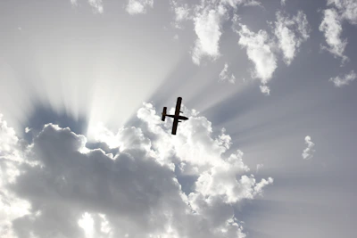 Silhouette of a small aircraft climbing into a bright blue sky at dawn.