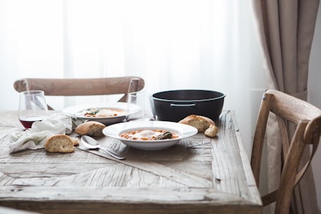 Close-up of a rustic wooden table set with steaming bowls of hearty soup and fresh bread.