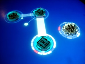 A digital interface featuring glowing blue circular icons with different symbols. The icons are connected through a bright line on a smooth blue surface, resembling a futuristic touch screen. Intricate designs and circuit-like patterns can be seen within the icons.