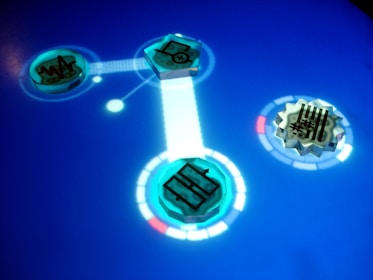 A digital interface featuring glowing blue circular icons with different symbols. The icons are connected through a bright line on a smooth blue surface, resembling a futuristic touch screen. Intricate designs and circuit-like patterns can be seen within the icons.
