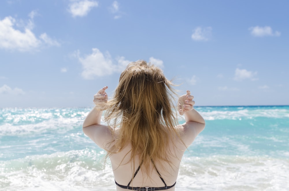 femme portant un soutien-gorge noir levant les deux bras face à la mer pendant la journée