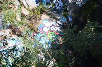 A vibrant graphic tee featuring a melting monster in toxic green, hot pink, and electric purple on a dark purple background.