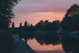 A serene riverside scene at sunset with a wooden footbridge and lush tropical forest.
