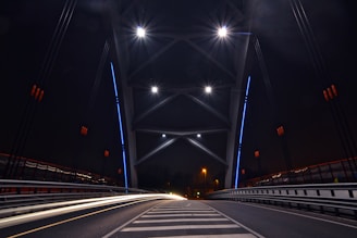 Nighttime image of a lit-up urban bridge highlighting its architectural design and structural lines.