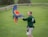 A person wearing a green ZSL sweatshirt stands on a grassy field, interacting with a vibrant macaw bird in flight. The macaw's wings are fully spread, showcasing its colorful red, yellow, and blue feathers.