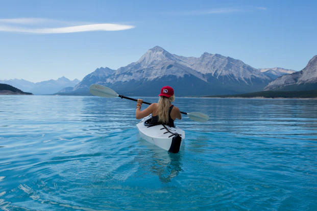 Traveler kayaking across a clear mountain lake surrounded by dramatic peaks.