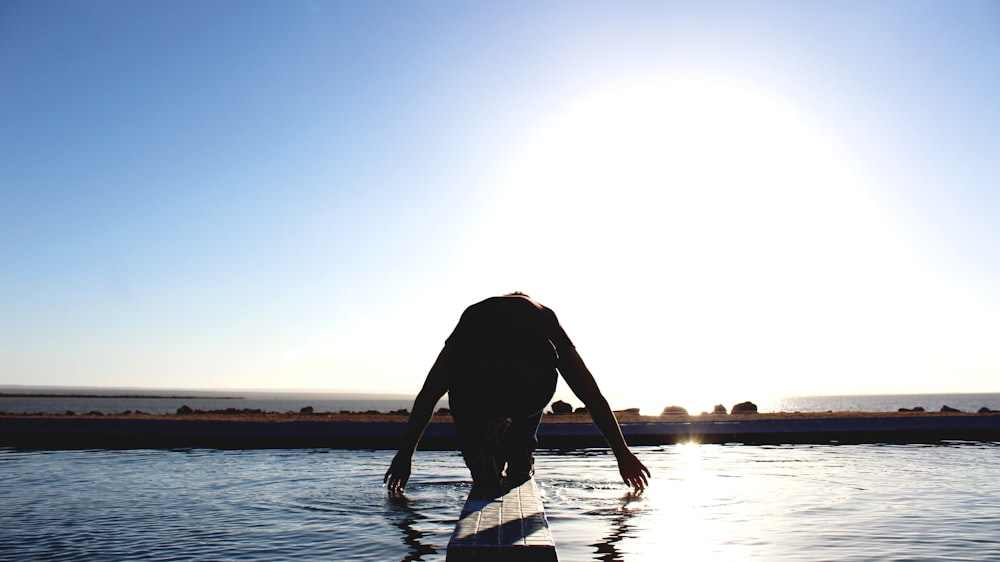 person kneeling on wood surface surrounded by body of water