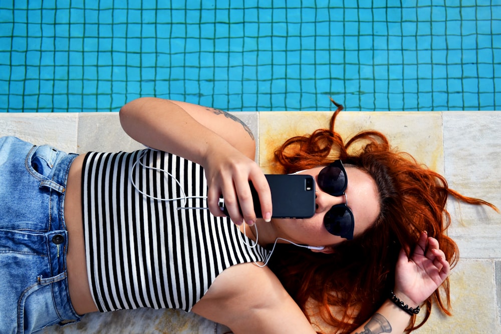 Sunglass wearing woman relaxing near swimmingpool with earphone plugged in iPhone at Sao Paulo