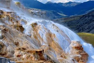 A stunning landscape showcasing colorful mineral terraces formed by cascading thermal waters, set against the backdrop of rugged mountains and rolling hills.