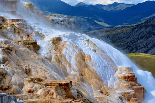 A stunning landscape showcasing colorful mineral terraces formed by cascading thermal waters, set against the backdrop of rugged mountains and rolling hills.