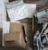 An assortment of stationery and knitting materials spread out on a textured wooden surface. Various items include patterned paper, envelopes with botanical designs, a black pen, and sheets with grid patterns. A knitting project is in progress, featuring yarn and knitting needles, which adds a cozy texture to the scene.