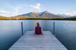 woman sitting on dock bridge near lake during daytime