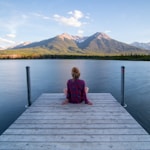 woman sitting on dock bridge near lake during daytime