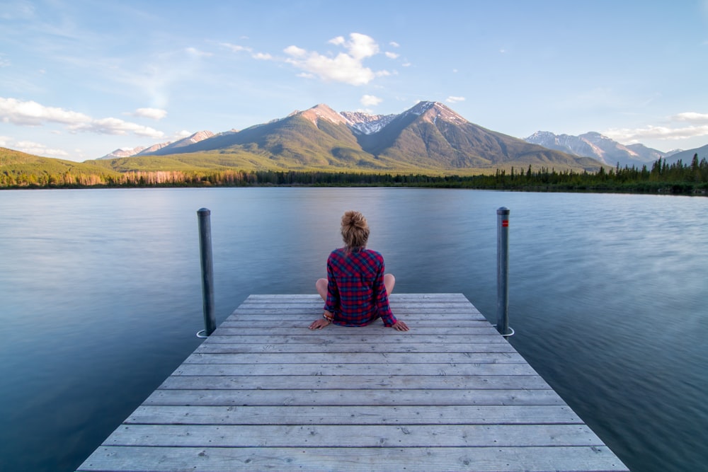woman sitting on dock bridge near lake during daytime