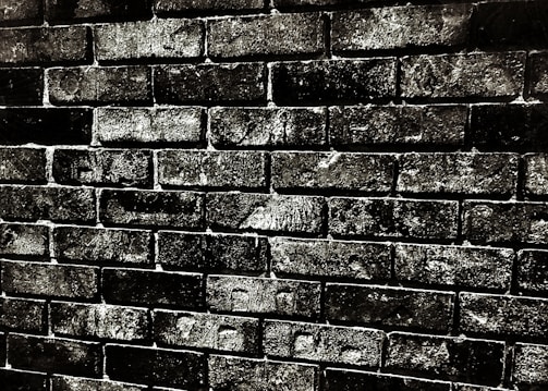 Rough-textured brick wall with dark mortar lines, showcasing an aged, worn appearance.