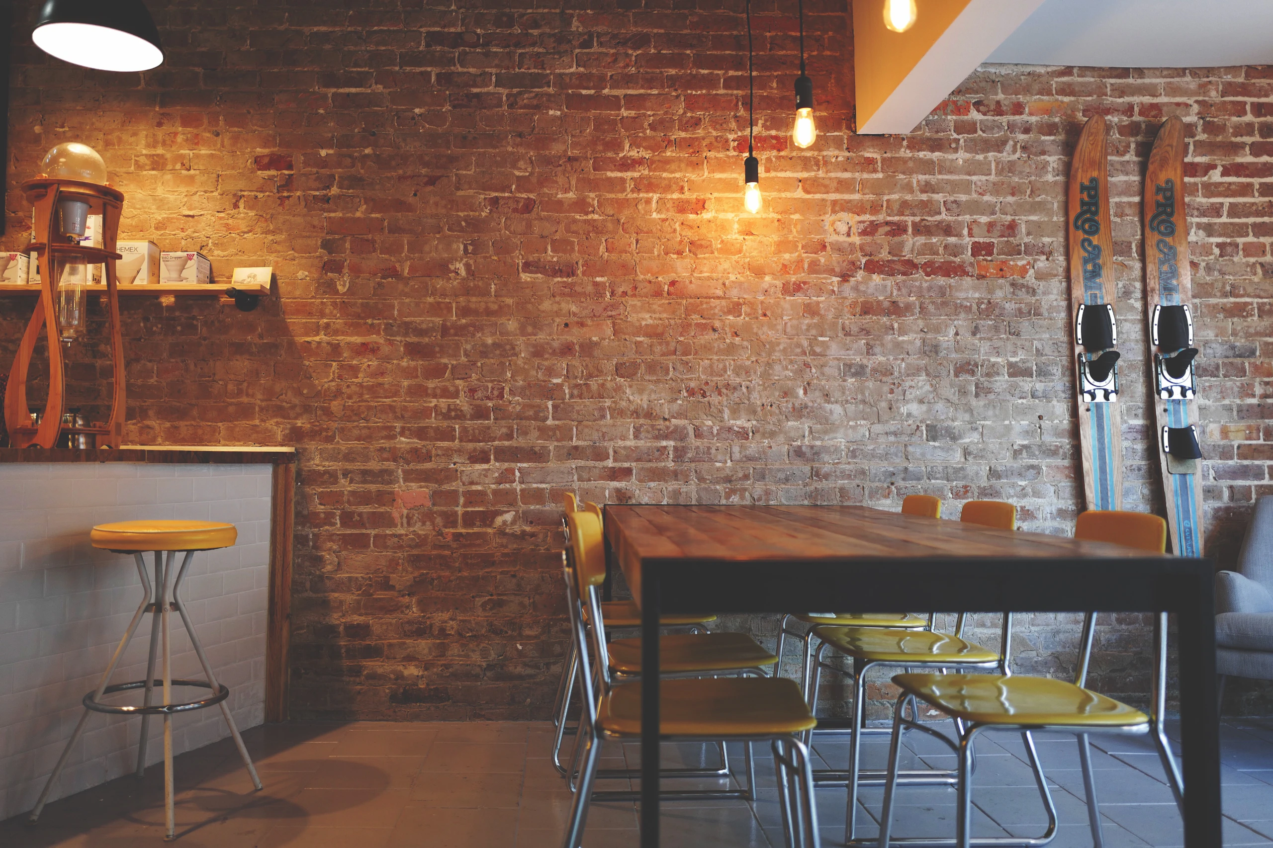 Cafe corner with exposed brick wall, wooden table and wire chairs